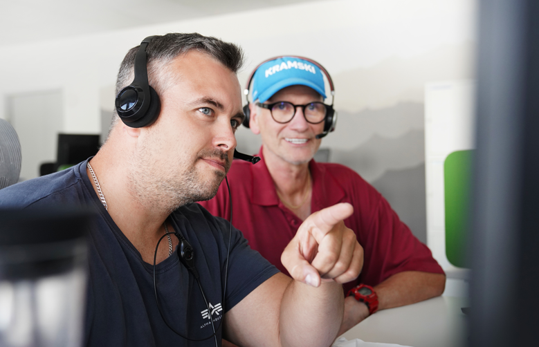 Zwei Mitarbeiter von PropertyExpert mit Headset, die auf einen Bildschirm schauen, einer von ihnen deutet auf den Bildschirm