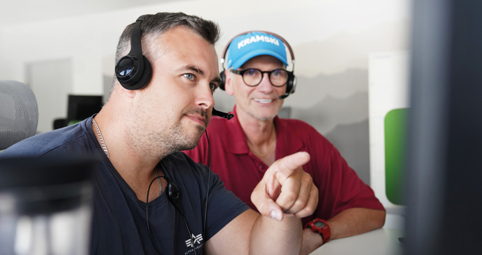 Zwei Mitarbeiter von PropertyExpert sitzen mit Headsets vor einem Bildschirm.