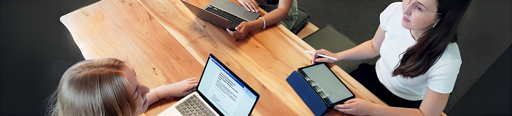 Mehrere Mitarbeiterinnen von PropertyExpert sitzen mit Laptops und einem iPad an einem Holztisch, darunter Emilia Heitmann
