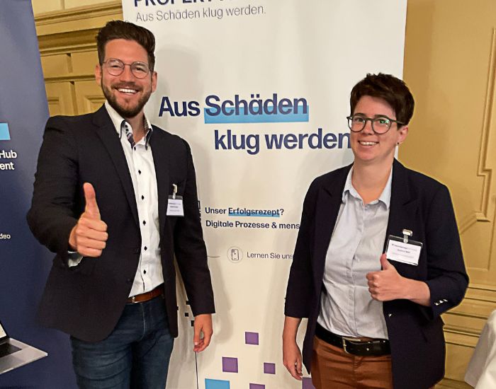 Dennis Kelput (PropertyExpert) und Andrea Woll (Neodigital) stehen mit Daumen hoch vor einem Aufsteller von PX