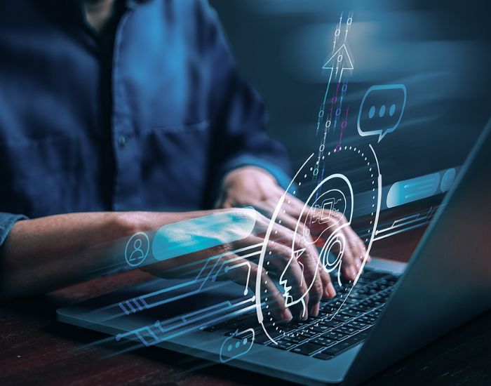 Mann tippt auf auf Laptop-Tastatur, davor technische Einblendungen mit Bezug zu künstlicher Intelligenz